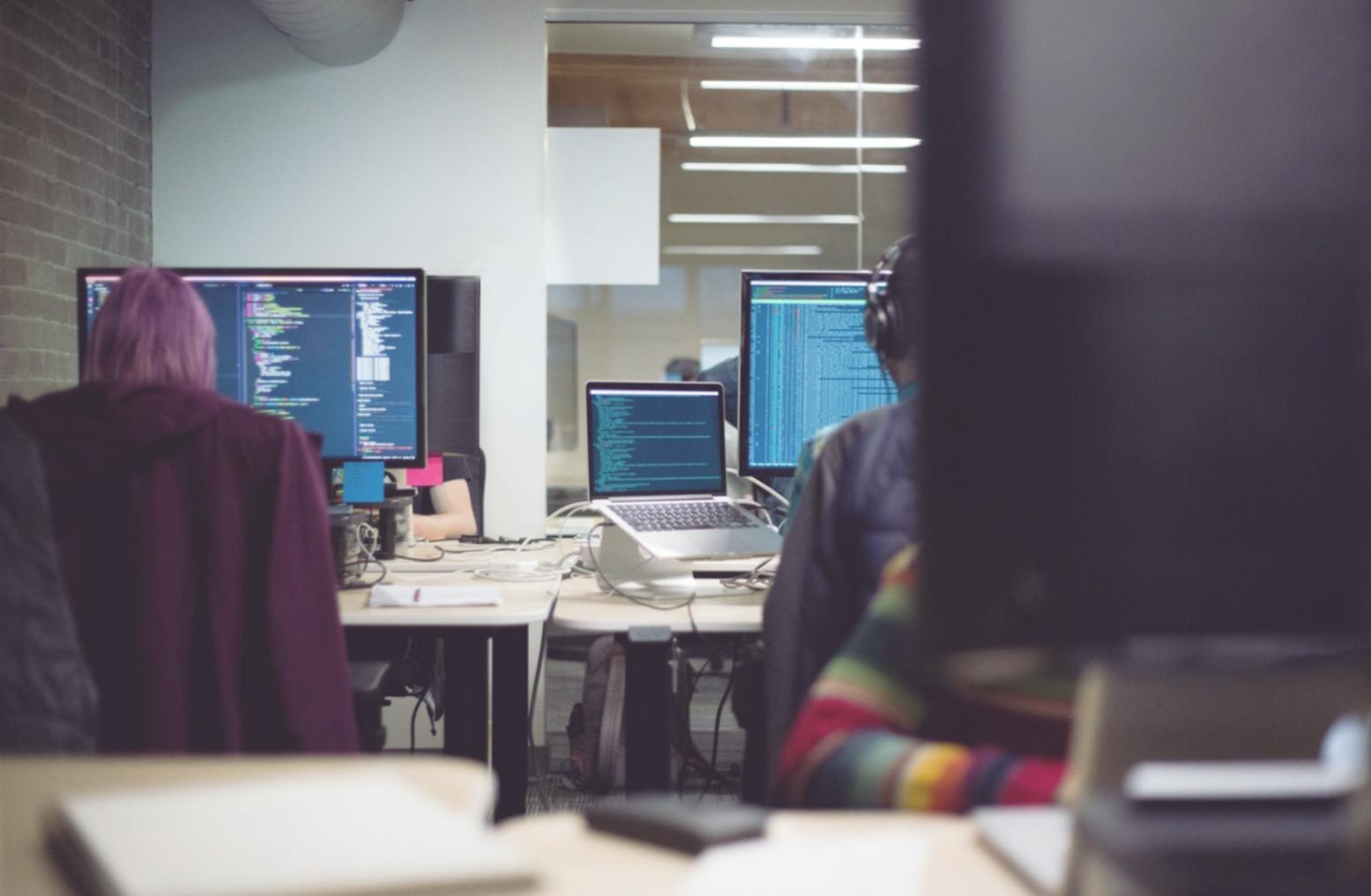 Network engineer reviewing system logs and performance metrics on multiple monitors